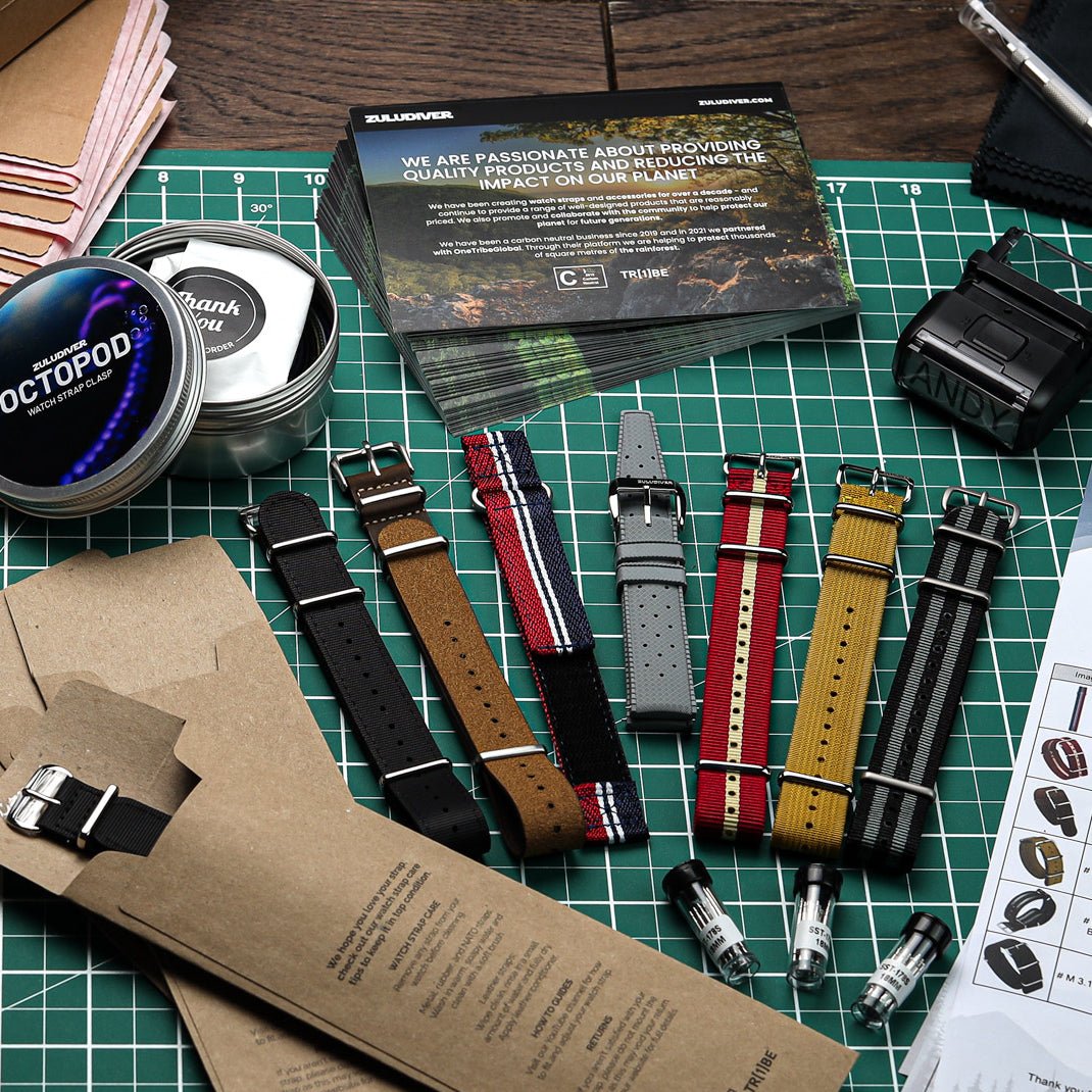 A variety of items laid out on a table, including watch straps, gift cards, gift boxes being packed for a ZULUDIVER customer order.