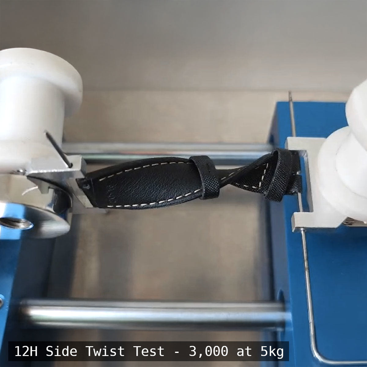 Black strap undergoing a side twist test with measurement details on a metallic background