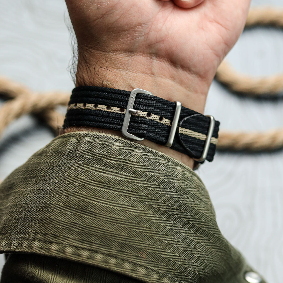 Person wearing a black and beige woven strap with a metal buckle on a blurred background