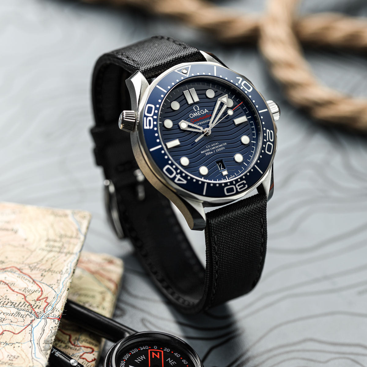 Omega watch with blue dial and black strap on a textured surface with map and compass.