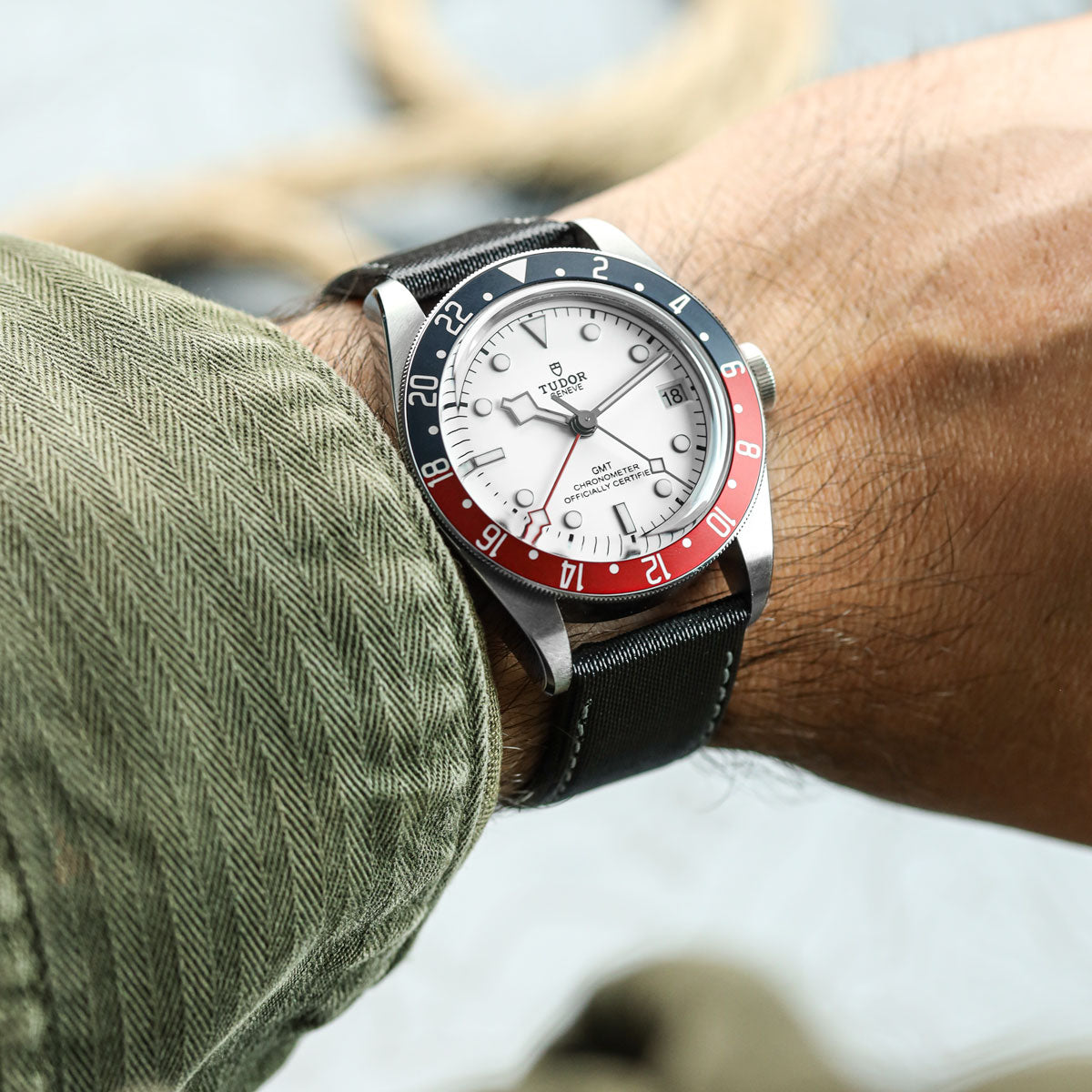 Close-up of a person wearing a Tudor watch with a red and blue bezel, fitted to Maverick sailcloth watch strap with grey stitching