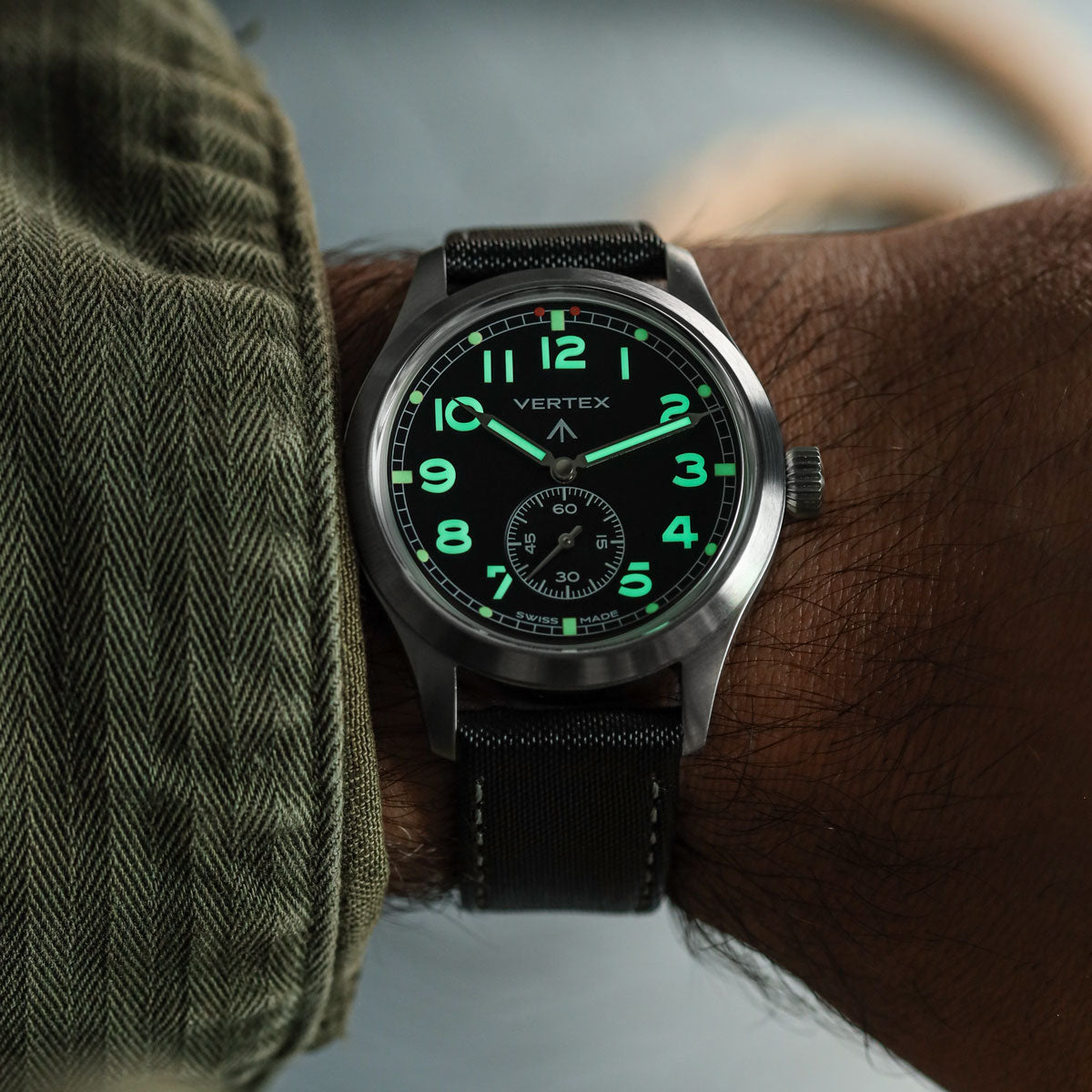 Vertex watch with green glowing lume on a wrist, brand &#39;Vertex&#39; visible, fitted to Maverick sailcloth watch strap with grey stitching